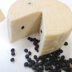 Vegan Gondino Peppercorn Parmesan Cheese Alternative by Pangea Foods served with whole black peppercorns.