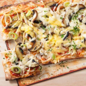 Vegan Grated Original Cheese Alternative by Violife melted onto pizza with mushrooms, spring onions and Violife Mozzarella.