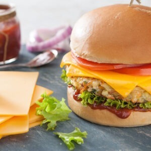 Vegan Cheddar Cheese Alternative Slices by Violife served in a burger pun with a vegetable patty, lettuce, tomatoes and relish.