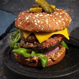 Vegan Mature Cheddar Cheese Alternative Slices by Violife served in a burger bun with a grilled mushroom, salad leaves, red onion, gherkins, mustard and relish.