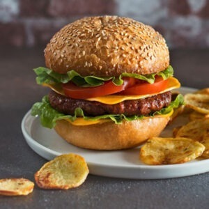 Vegan Cheddar Cheese Alternative Slices by Greenvie served in a burger bun with a vegan burger patty, tomato, salad and grilled potato slices.