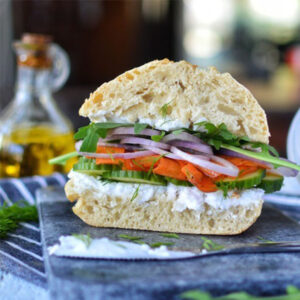 Vegan Creamy Original Spread by Greenvie served in bread with cucumber, tomato, red onion and rocket.