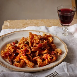 Vegan Puttanesca Pasta Sauce by Seggiano served with pasta and olives, with a glass of wine.