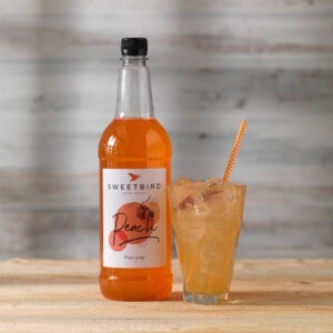 Vegan Peach Fruit Syrup by Sweetbird served in a cool drink with ice and peach.