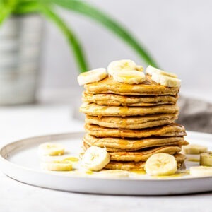 Vegan Pancake Mix by Just Wholefoods served as a pancake stack with syrup and fresh sliced banana.