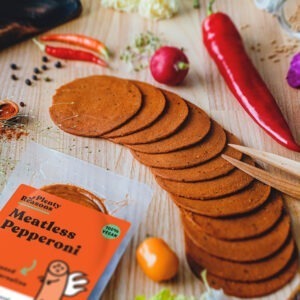 Vegan Pepperoni Slices by Plenty Reasons shown on a table with peppers, chillies and radish.