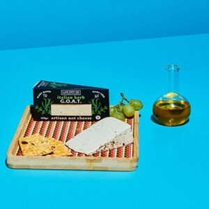 "G.O.A.T" Italian Herbs wedge by I Am Nut OK served on a cheeseboard with crackers and grapes.