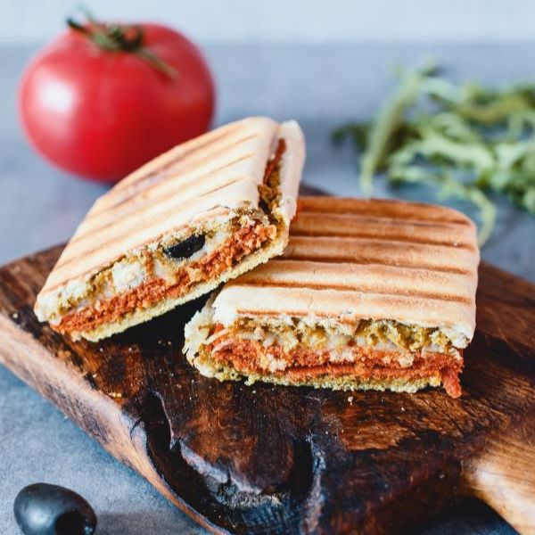 Vegan Salami Picante by Plenty Reasons shown in a panino with olives and vegan cheese.