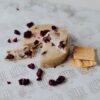 Vegan Aged with Cranberry by Nutty Artisan Co shown next to dried cranberries and some crackers.