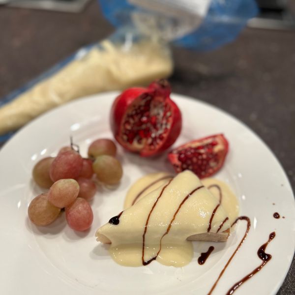 Vegan TiVamisù Cream by The Alternative Food served over a slice of cake with a chocolate sauce drizzle and some fresh fruit.