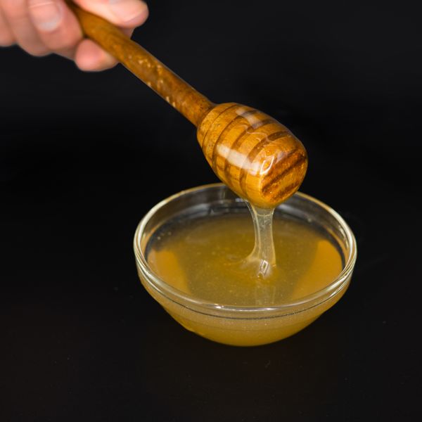 Vegan H*ney by Better Foodie shown in a glass dish with a wooden honey dipper.