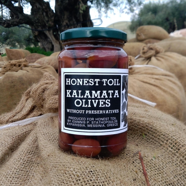Vegan Kalamata Olives by Honest Toil. Jar shown on sacks in an olive grove.