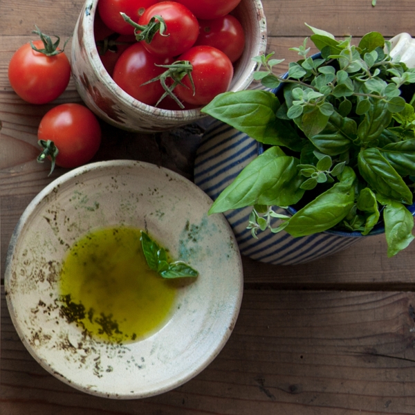 Vegan Unfiltered Extra Virgin Olive Oil by Honest Toil. Shown next to fresh tomatoes and basil.